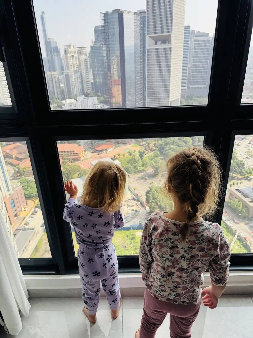 children looking out over Kuala Lumpur skyline from a family apartment near KLCC during a Malaysia itinerary with kids