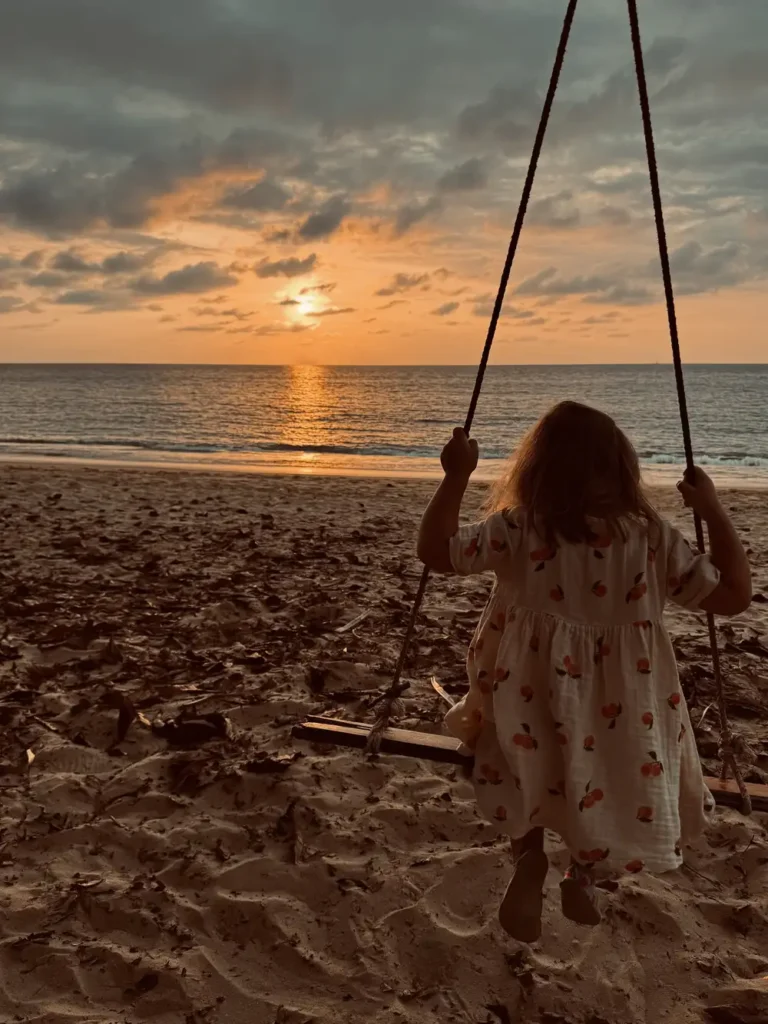 Kind geniet van de zonsondergang op een schommel aan het strand van Khao Lak, Thailand