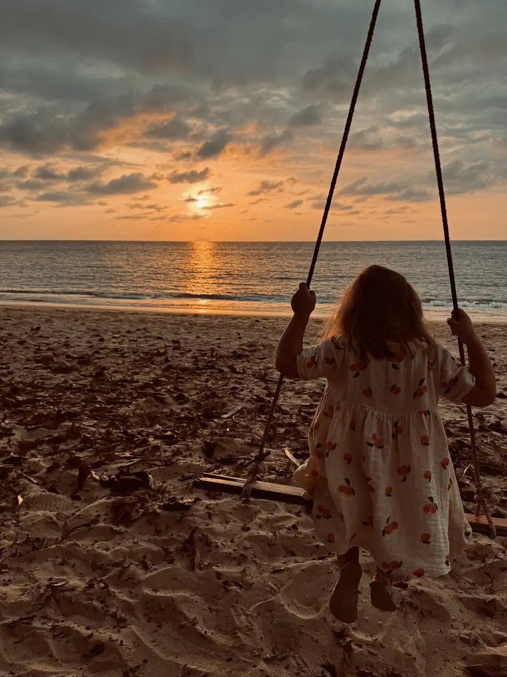 Kind geniet van de zonsondergang op een schommel aan het strand van Khao Lak, Thailand