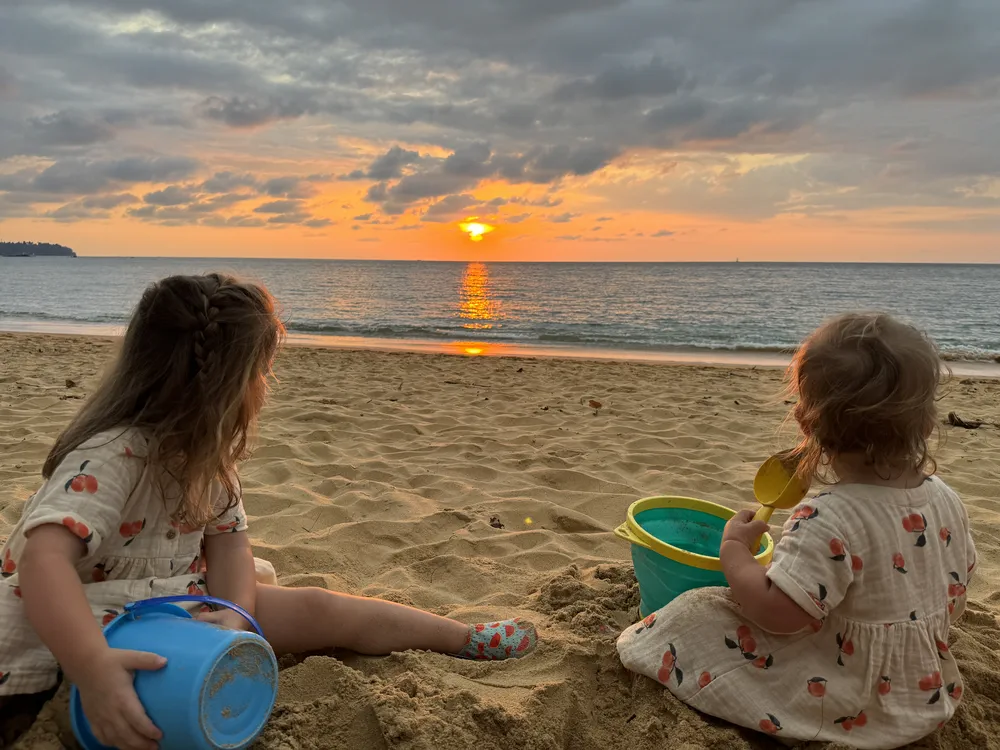 Peuter en baby spelen in het zand bij zonsondergang op Khao Lak beach
