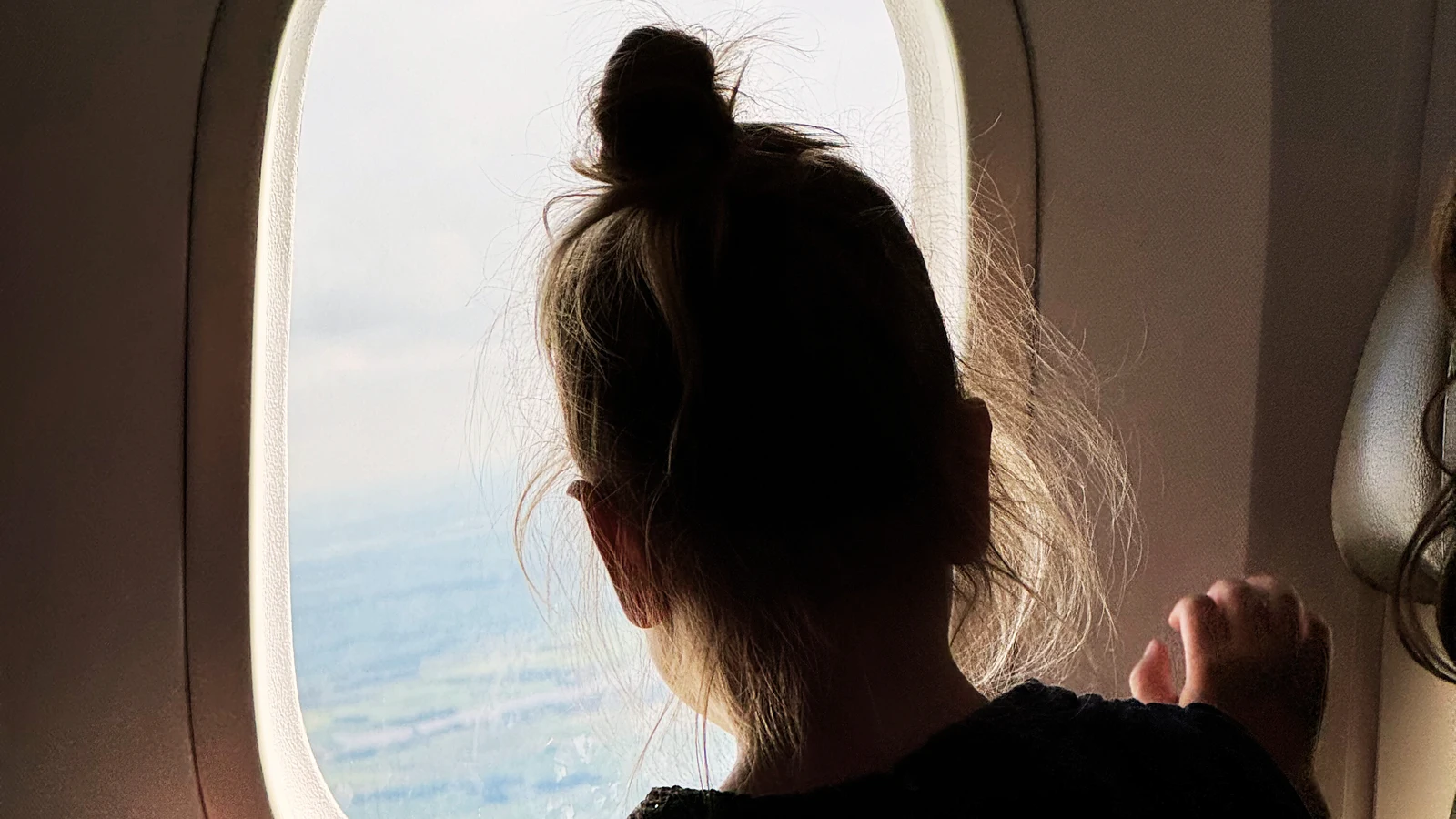 Child looking out airplane window during long flight with kids