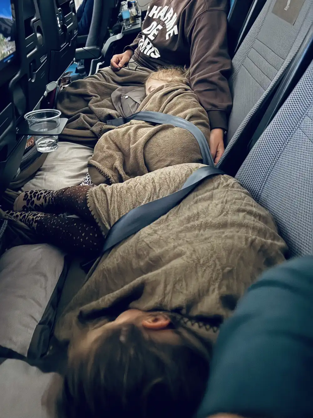 Sisters sleeping across airplane seats during a long-haul flight